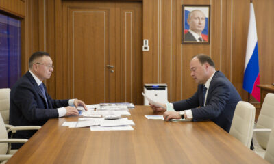 Совещание двух чиновников за столом с документами в кабинете с российским флагом
