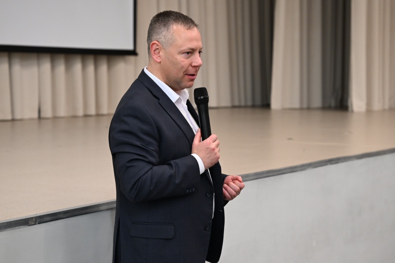 Мужчина в деловом костюме выступает с микрофоном на сцене