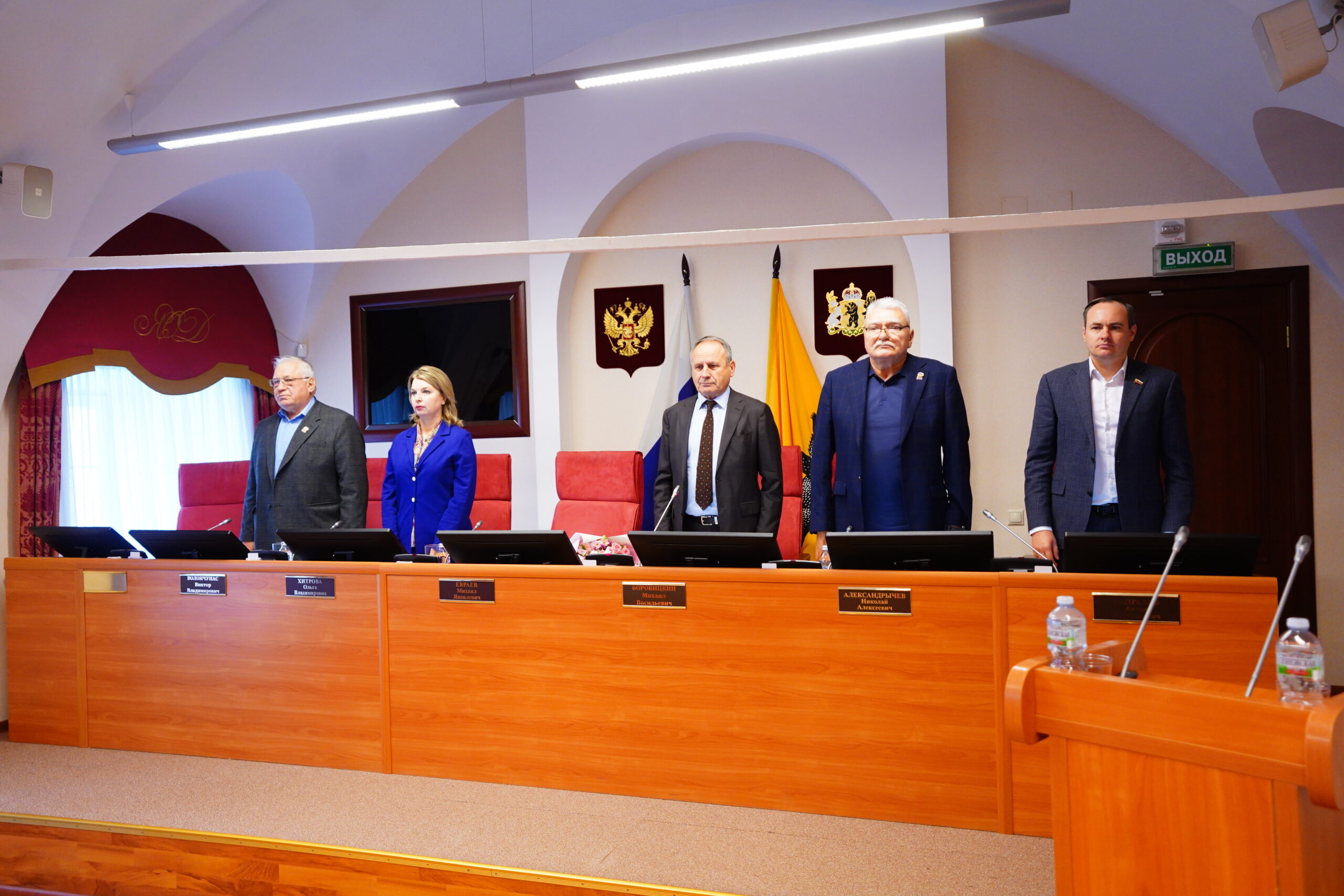 Депутаты областной думы стоят в зале заседаний во время минуты молчания