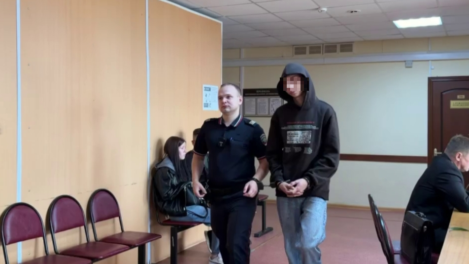 Сотрудник полиции сопровождает мужчину в капюшоне по коридору суда