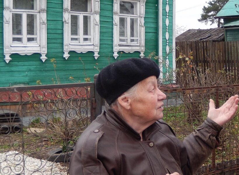 Пожилая женщина у зелёного деревянного дома с резными наличниками