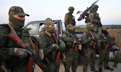 Вооружённые военнослужащие в камуфляже стоят у пикапа в поле