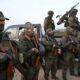 Вооружённые военнослужащие в камуфляже стоят у пикапа в поле
