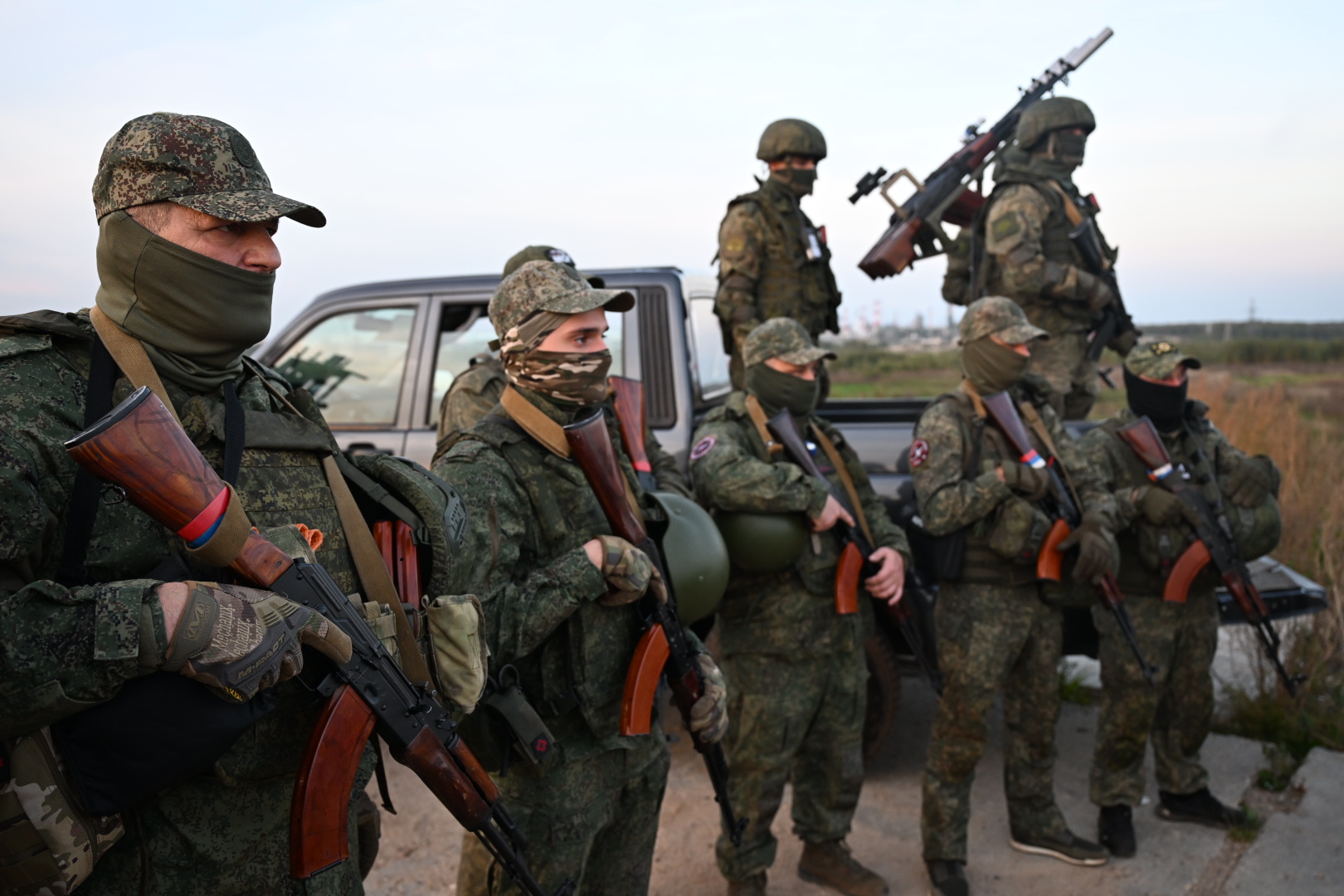 Вооружённые военнослужащие в камуфляже стоят у пикапа в поле