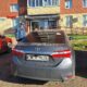 Серая Toyota Corolla у жилого дома, рядом стоит сотрудник в форме
