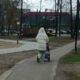 Женщина в белой куртке идет по тротуару с детской коляской