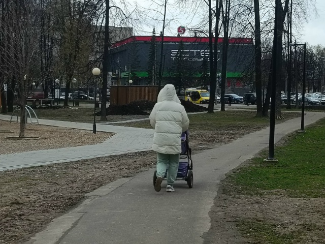 Женщина в белой куртке идет по тротуару с детской коляской
