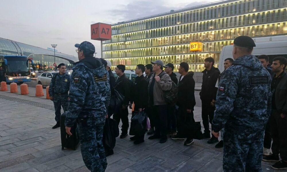 Сотрудники полиции сопровождают группу мужчин с багажом у автобусной остановки аэропорта
