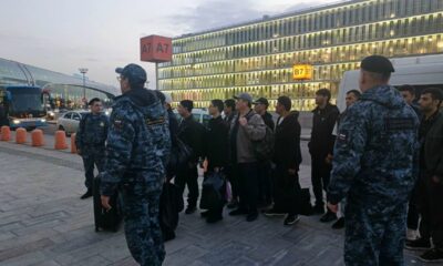 Сотрудники полиции сопровождают группу мужчин с багажом у автобусной остановки аэропорта