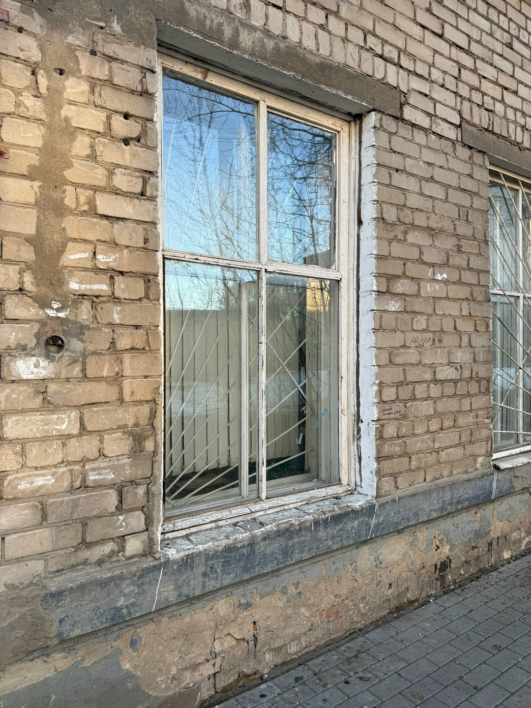 Окно с решёткой на фасаде многоквартирного дома из кирпича