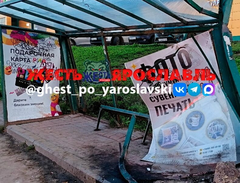 Повреждённая остановка с перекошенным рекламным щитом и разбитым тротуаром