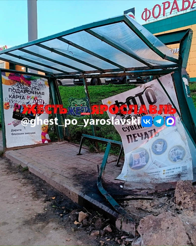 Повреждённая остановка с перекошенным рекламным щитом и разбитым тротуаром