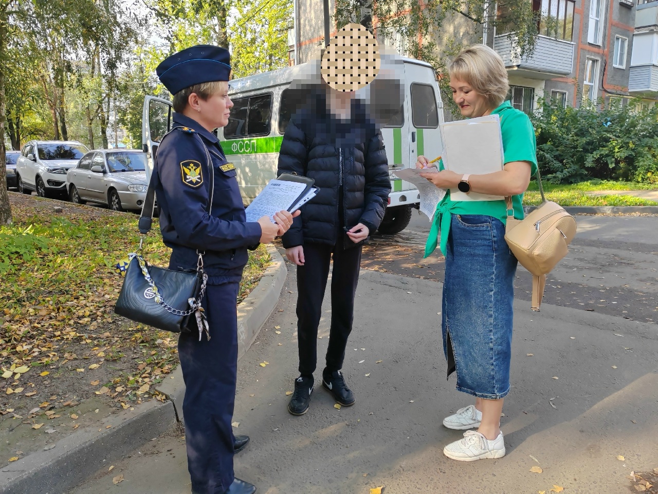 Судебный пристав беседует с женщиной и мужчиной с закрытым лицом у служебного автомобиля