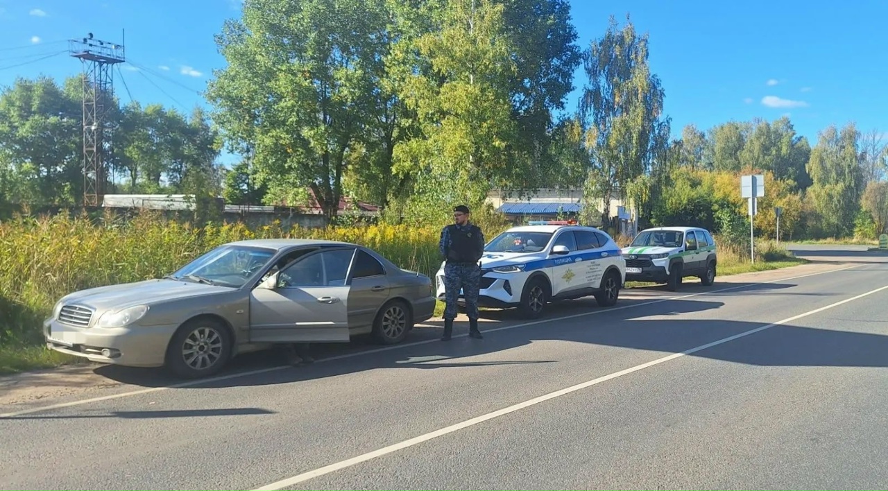 Сотрудник службы судебных приставов стоит у остановленного седана, рядом служебные автомобили
