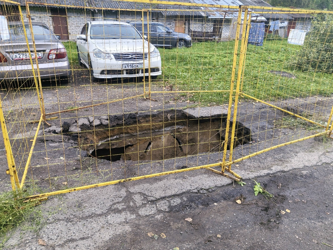 Провал перекрытия тепловой камеры на асфальте, огороженный жёлтым металлическим барьером