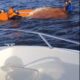 Спасатели в оранжевых жилетах помогают людям у перевернувшейся лодки на воде