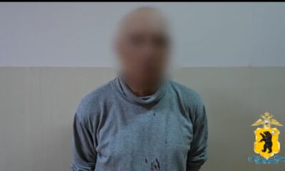 Мужчина с размытым лицом в серой одежде на фоне стены, рядом эмблема полиции