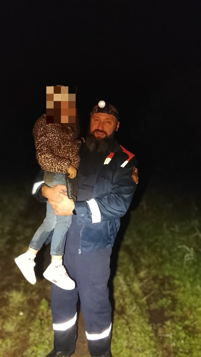 Спасатель с налобным фонарём держит на руках ребёнка с закрытым лицом ночью