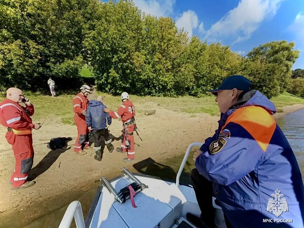Сотрудники МЧС и рыбак на берегу реки во время спасательной операции