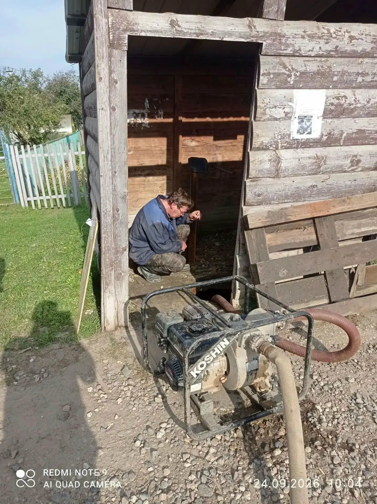 Мужчина обслуживает насос для подачи воды у деревянного дома в деревне