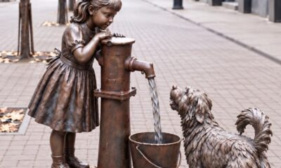 Бронзовая скульптура девочки с водяной колонкой и собакой на городской улице