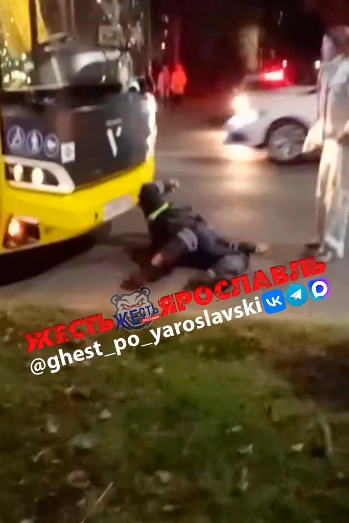 Сотрудник ДПС лежит на дороге у передней части жёлтого автобуса