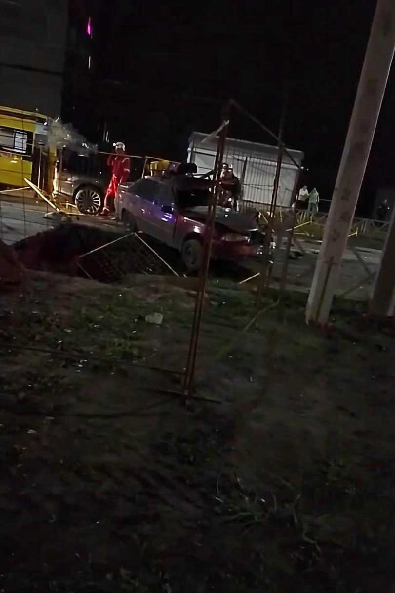 Автомобиль с повреждённым передом стоит у ограждённой коммунальной ямы ночью
