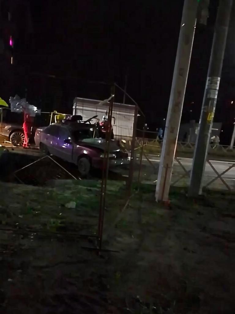 Автомобиль в коммунальной яме ночью, рядом работают спасатели