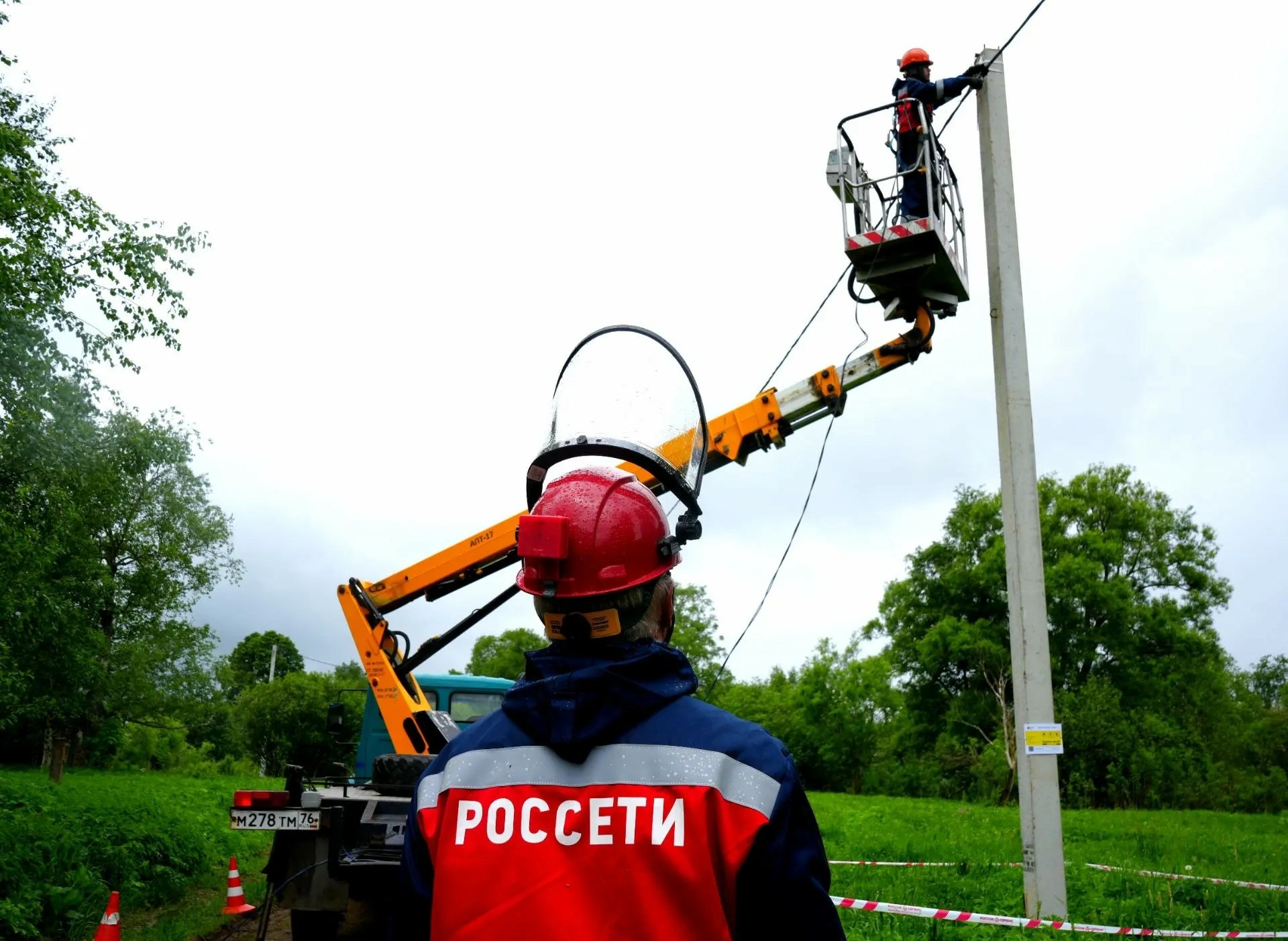 Энергетик Россети наблюдает за работой коллеги на автовышке у опоры линии электропередачи
