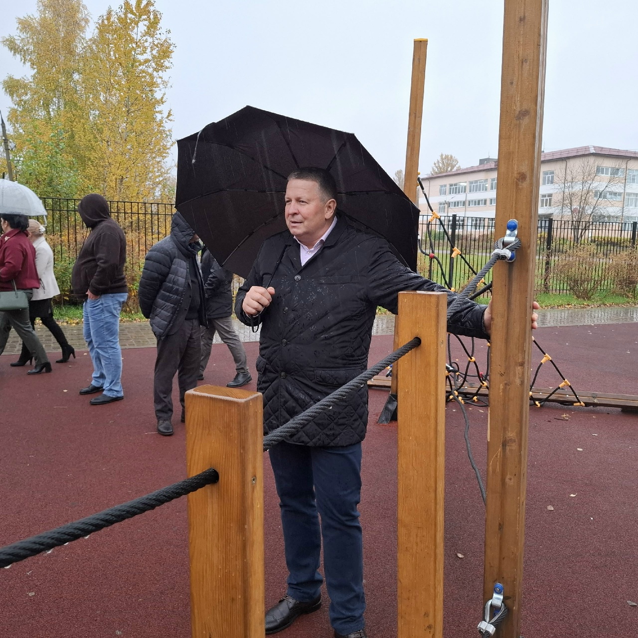 Мужчина с зонтом осматривает детскую площадку под дождём