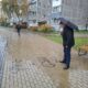 Мужчина с зонтом осматривает надписи вандалов на тротуаре у жилого дома