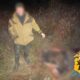 Мужчина в куртке стоит ночью рядом с размытым телом животного в траве