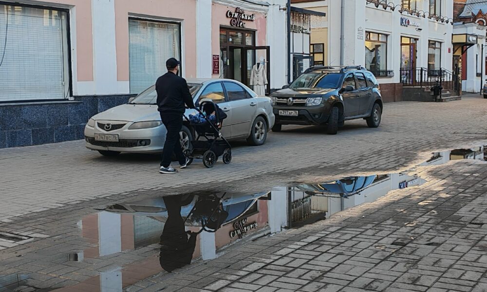 Мужчина везёт детскую коляску по тротуару рядом с припаркованными автомобилями