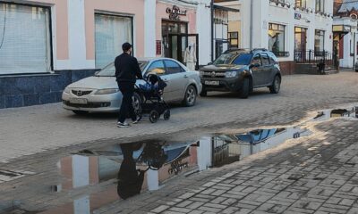 Мужчина везёт детскую коляску по тротуару рядом с припаркованными автомобилями