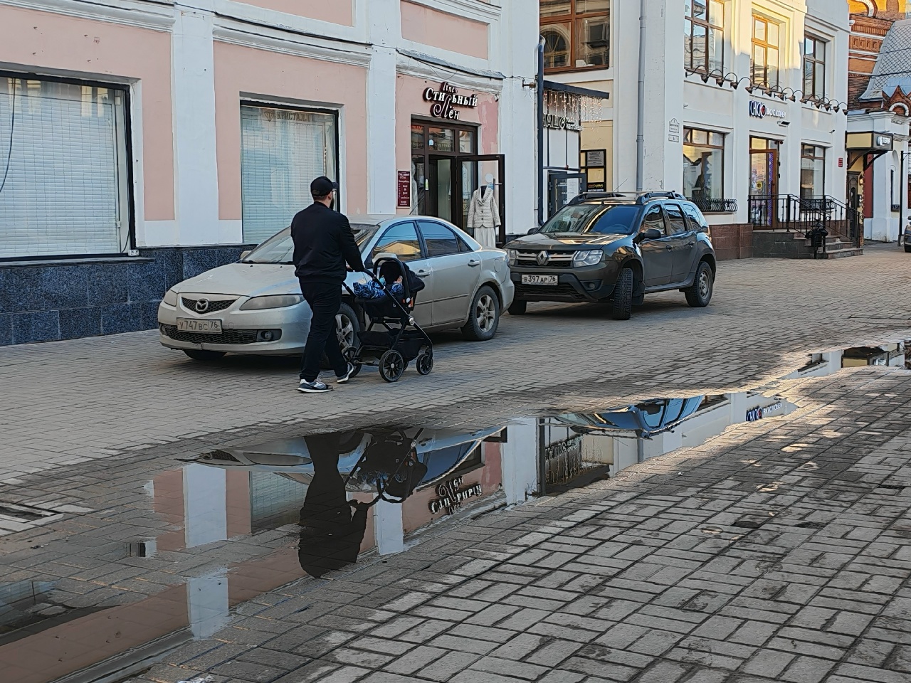 Мужчина везёт детскую коляску по тротуару рядом с припаркованными автомобилями