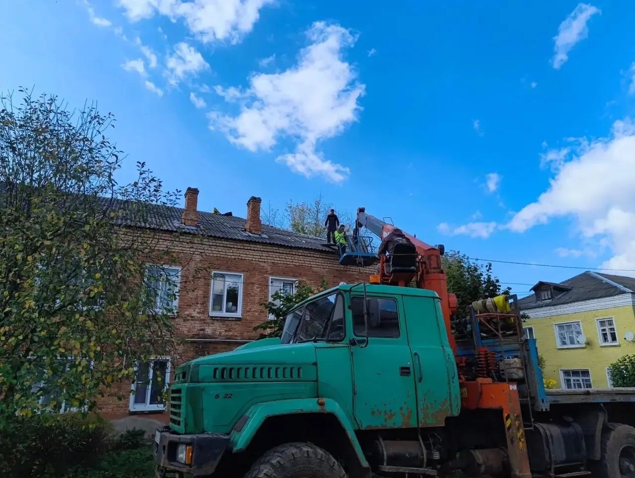 Рабочие ремонтируют крышу кирпичного дома с автовышки