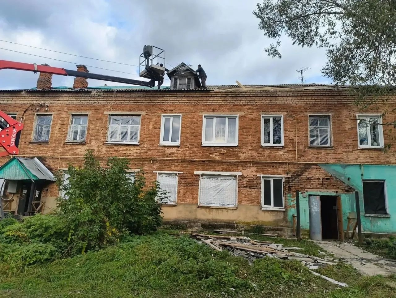 Рабочие ремонтируют крышу двухэтажного кирпичного дома с помощью автовышки