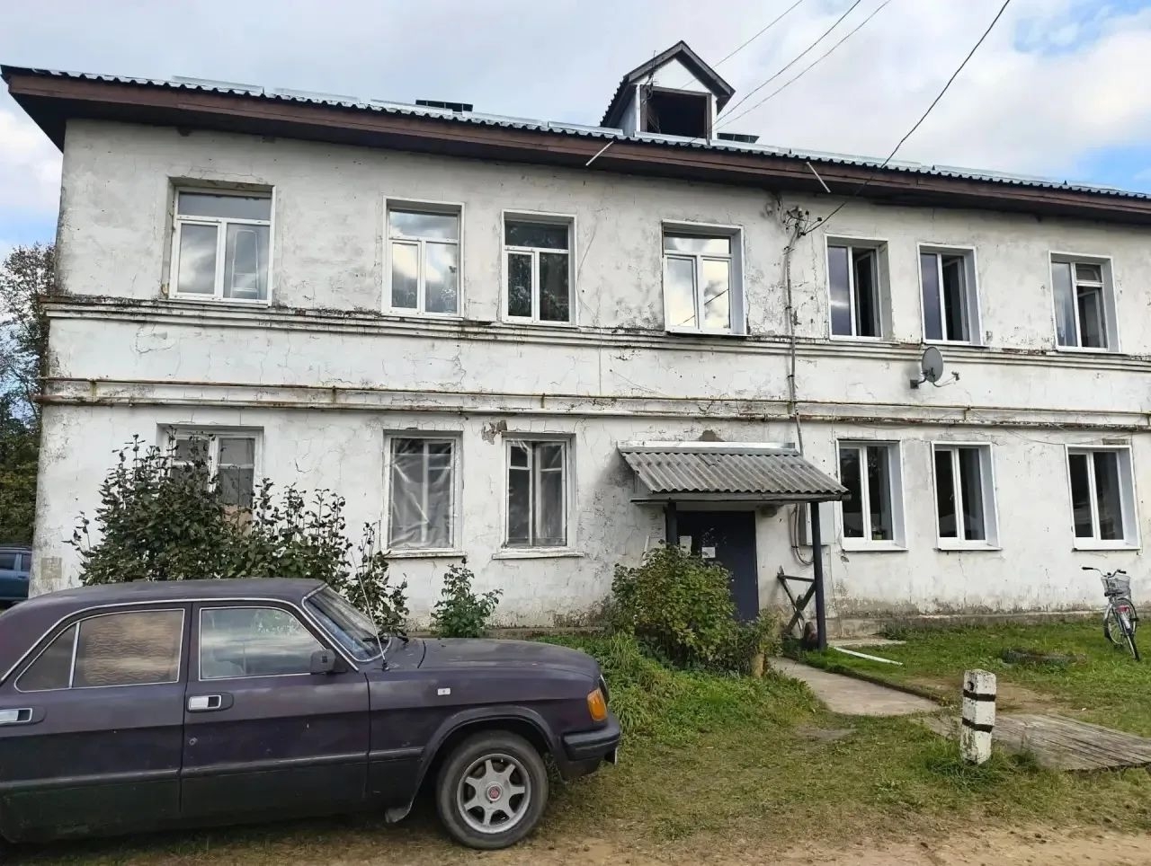 Двухэтажный жилой дом в Кубринске с трещинами на фасаде и припаркованным автомобилем