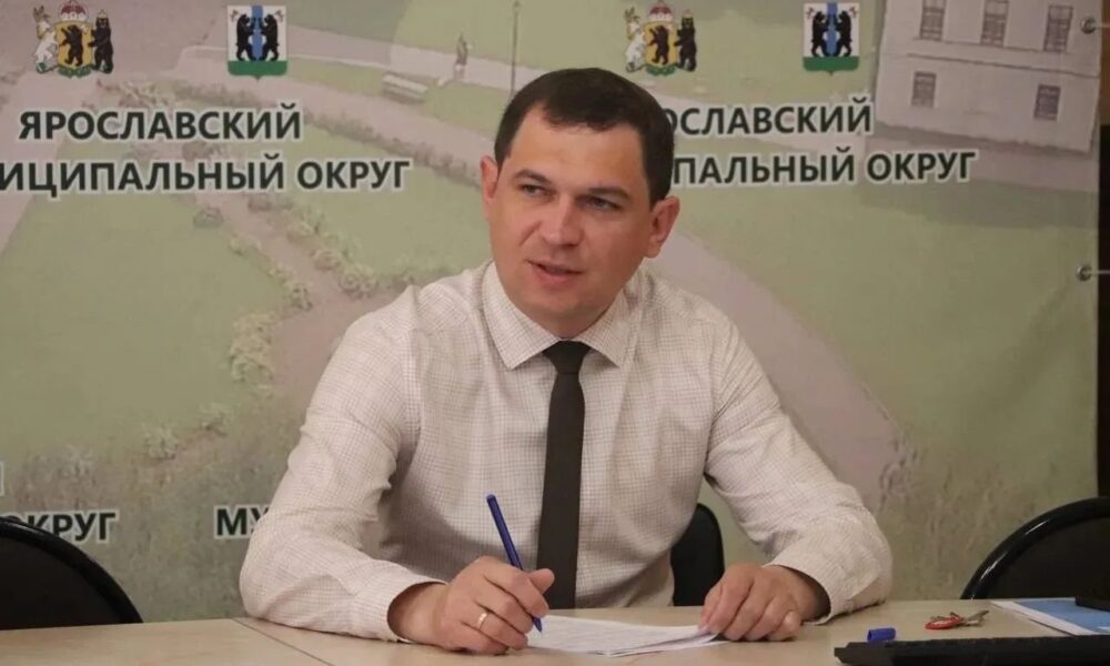 Мужчина в рубашке и галстуке подписывает документы на фоне баннера Ярославского муниципального округа
