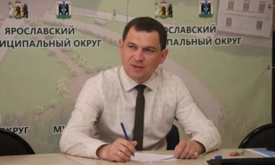 Мужчина в рубашке и галстуке подписывает документы на фоне баннера Ярославского муниципального округа