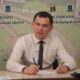 Мужчина в рубашке и галстуке подписывает документы на фоне баннера Ярославского муниципального округа