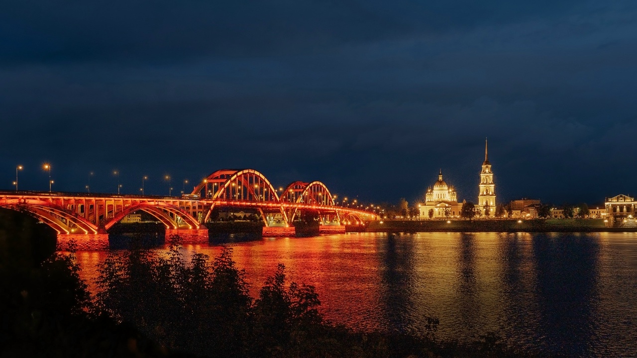 Волжский мост в Рыбинске с красно-золотой подсветкой ночью над рекой
