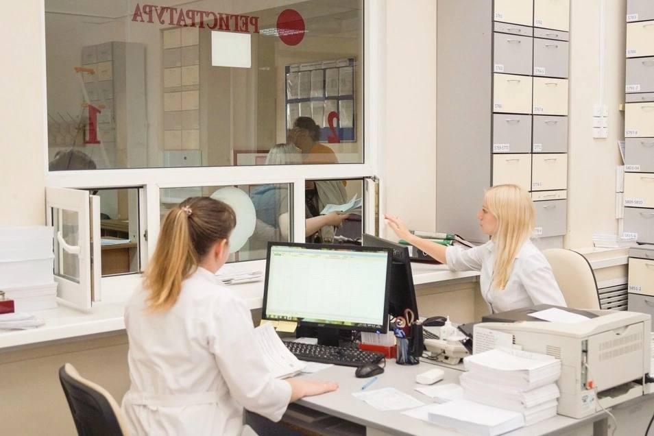 Регистратура поликлиники с сотрудницами за компьютером и медицинскими картами