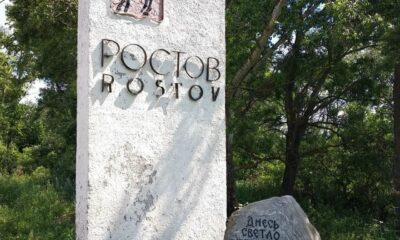 Въездная стела Ростова Великого с гербом и камнем у дороги среди деревьев