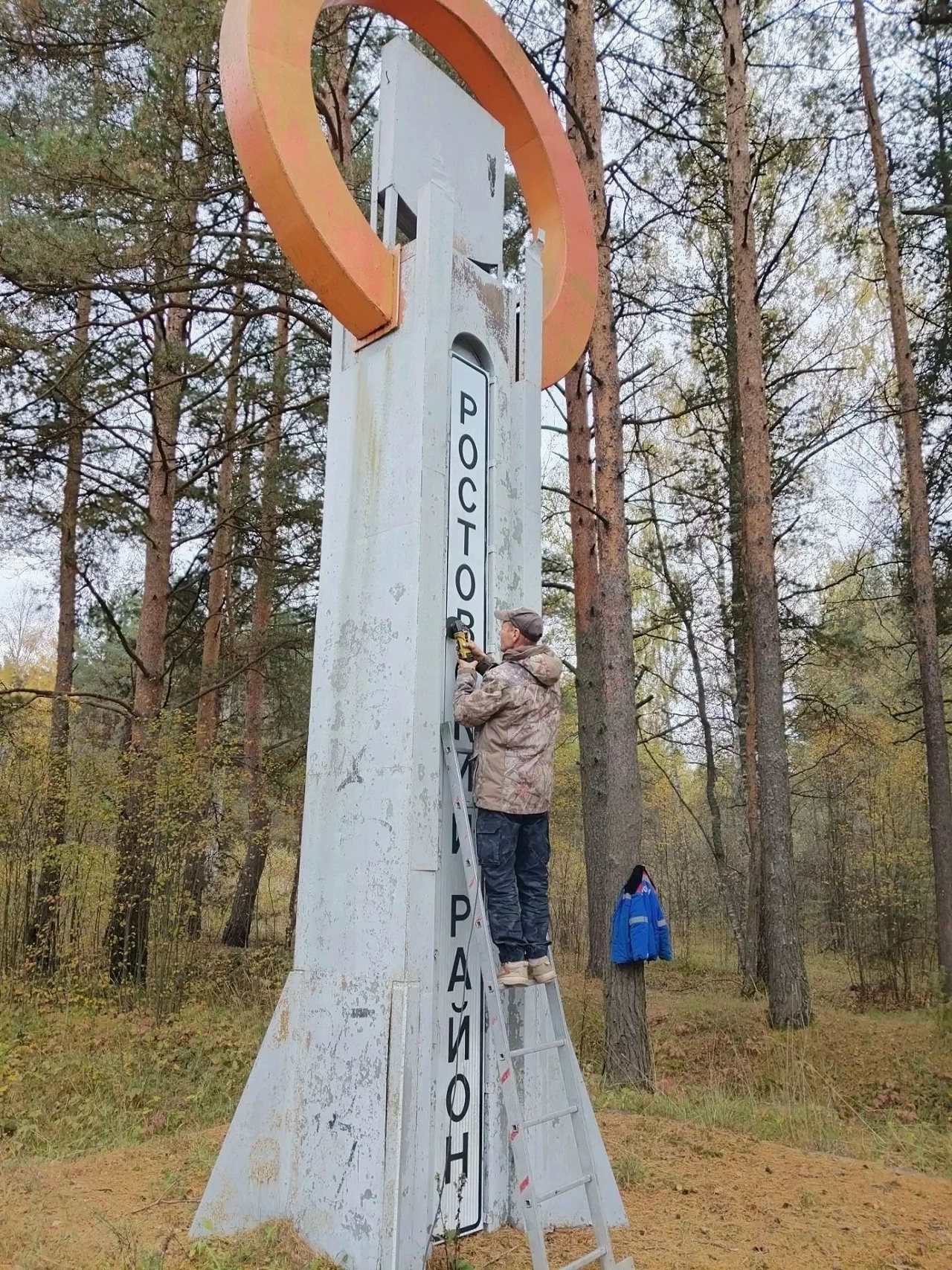 Рабочий на лестнице демонтирует буквы с въездной стелы Ростова Великого в лесу