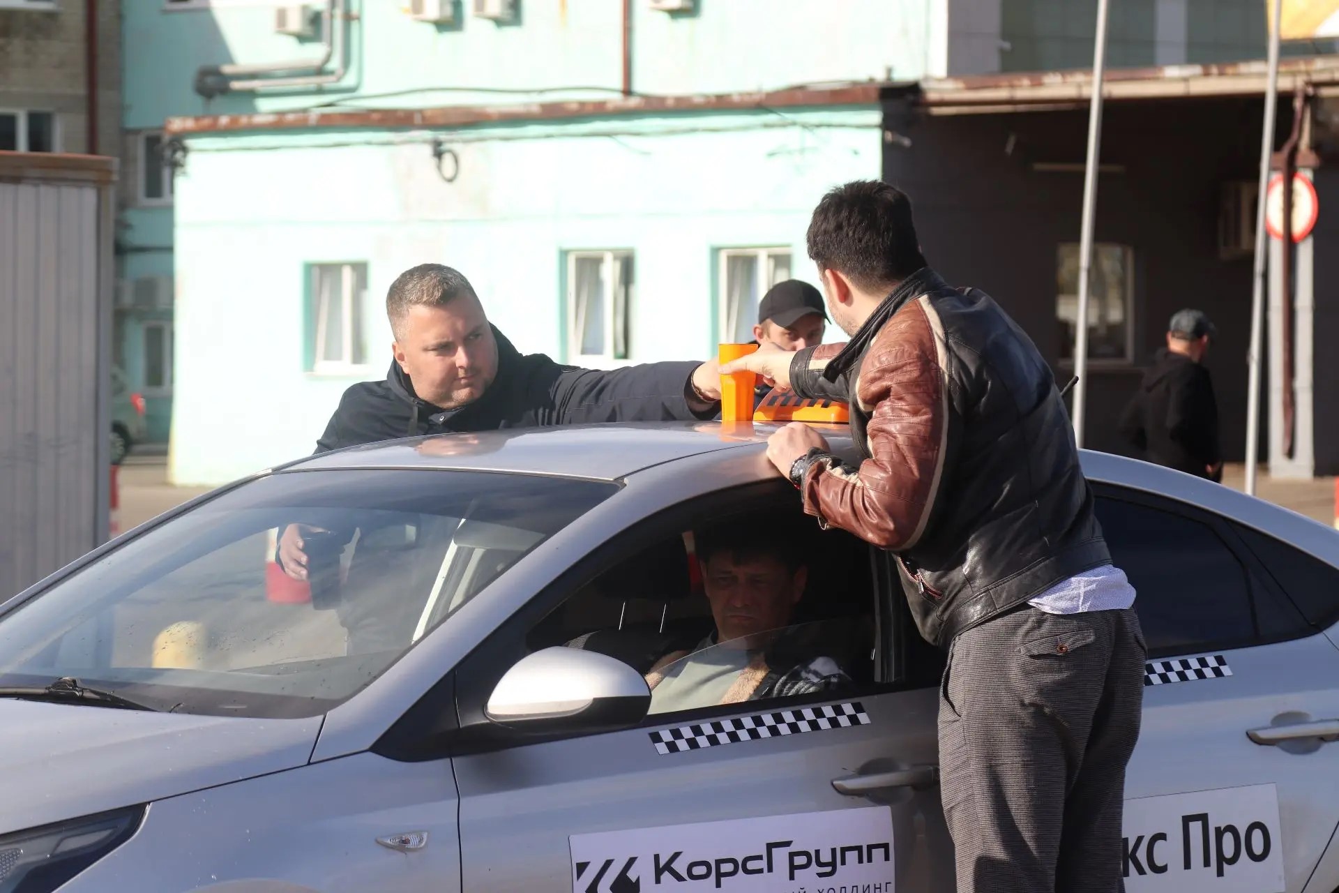 Таксист и мужчины ставят стаканы с водой на крышу автомобиля