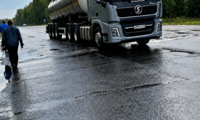 Грузовик-цистерна на мокрой разбитой дороге, рядом идут двое мужчин