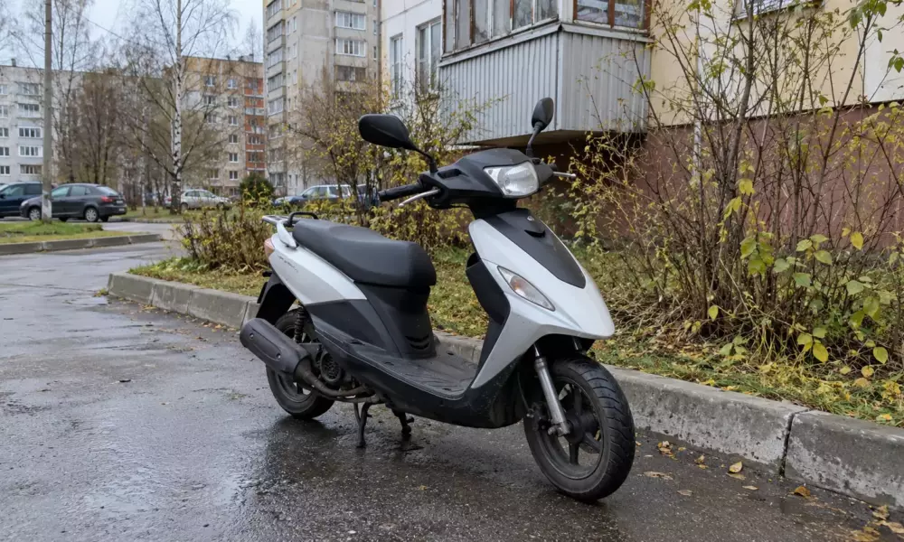 Серебристо-чёрный скутер у жилого дома на мокрой дороге