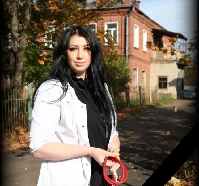 Женщина-врач в белом халате стоит на улице возле кирпичного здания