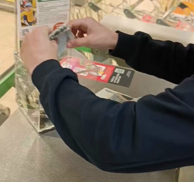 Человек кладет деньги в прозрачный ящик для сбора средств на лечение ребенка